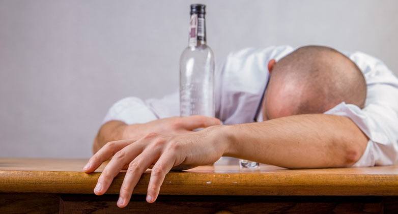 Man asleep at desk holding bottle with a hangover